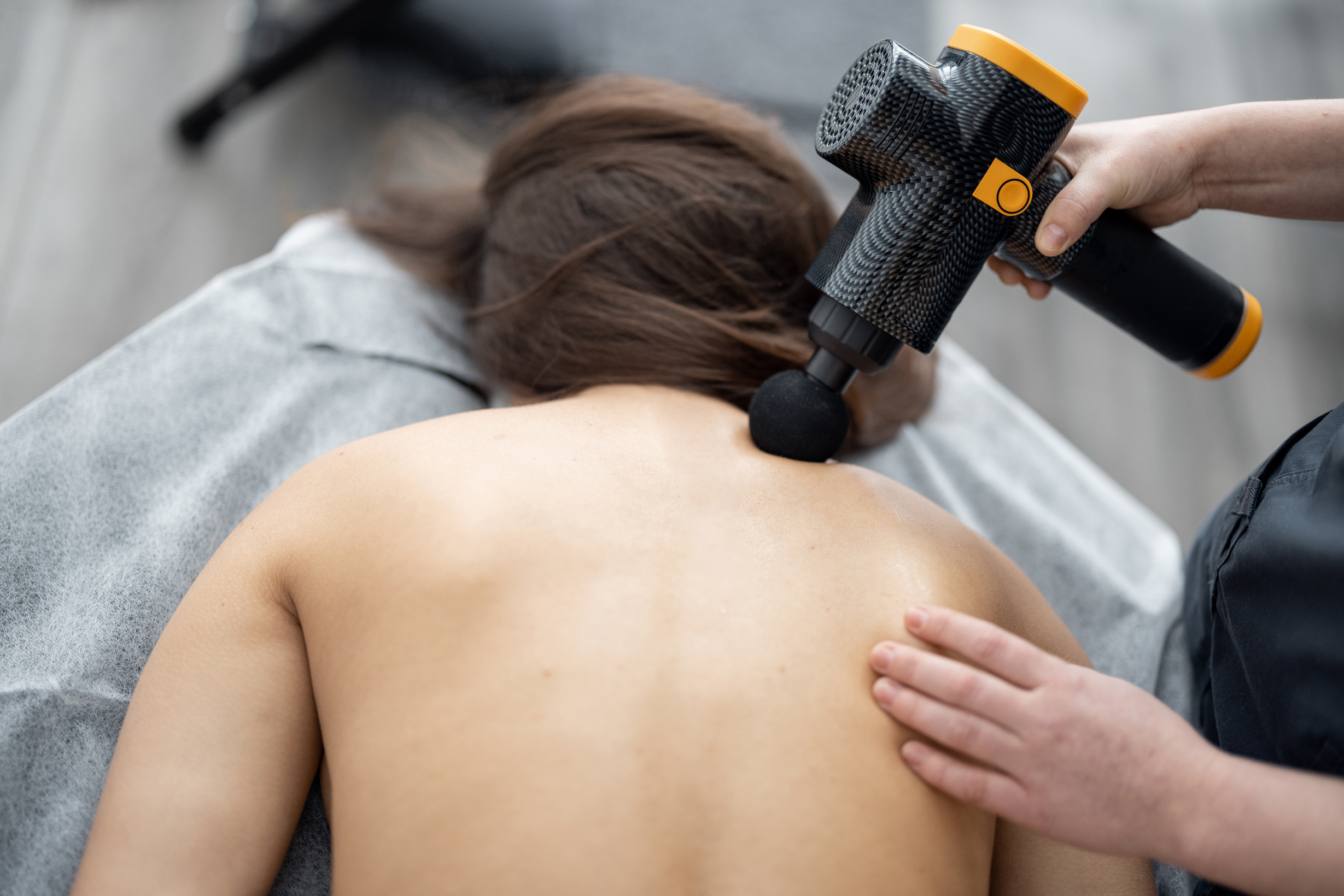 Masseuse Massaging Patient's Back with Percussion Massager